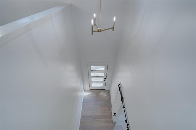 hall featuring a towering ceiling, light wood-style flooring, and a chandelier