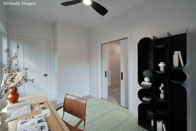 carpeted office space featuring ceiling fan and baseboards