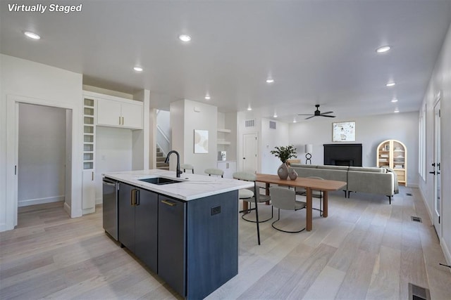 kitchen with a sink, white cabinetry, open floor plan, stainless steel dishwasher, and a center island with sink