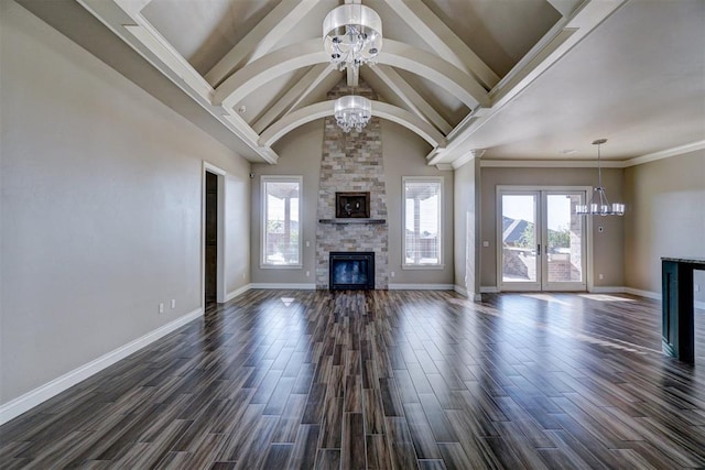 unfurnished living room with french doors, crown molding, an inviting chandelier, dark hardwood / wood-style floors, and a stone fireplace