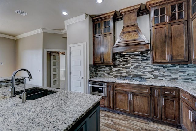 kitchen with light stone countertops, sink, stainless steel appliances, and custom range hood