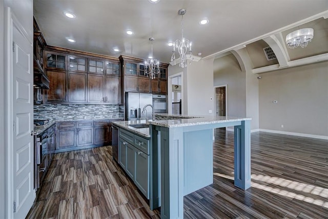 kitchen featuring light stone countertops, sink, hanging light fixtures, a center island with sink, and appliances with stainless steel finishes