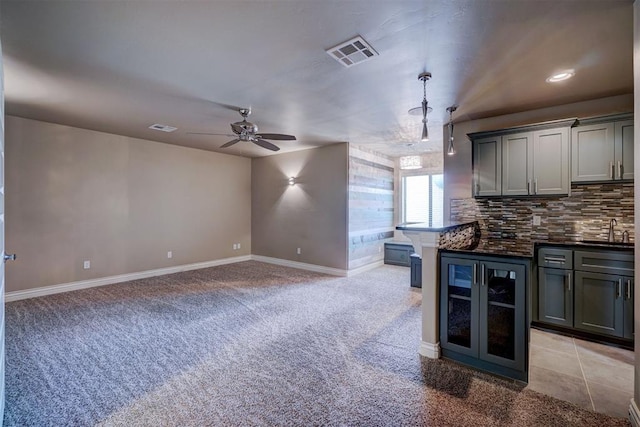 kitchen with gray cabinetry, ceiling fan, beverage cooler, backsplash, and light colored carpet