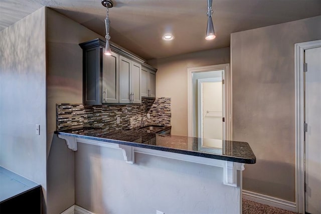 kitchen featuring pendant lighting, decorative backsplash, gray cabinets, a kitchen bar, and kitchen peninsula