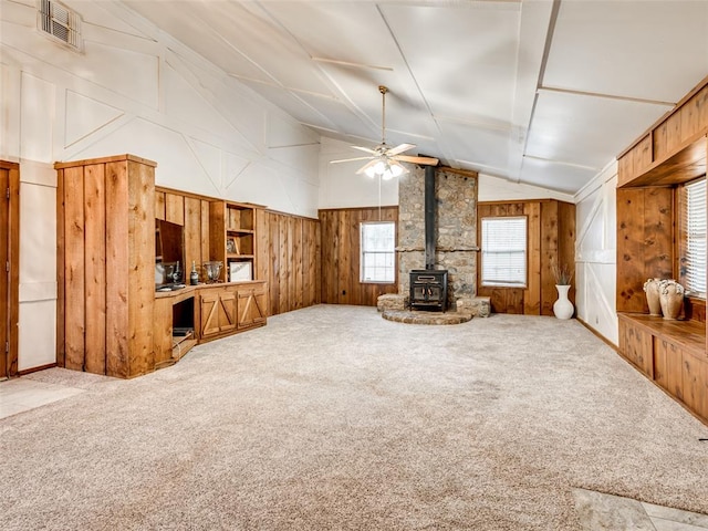 unfurnished living room featuring ceiling fan, wood walls, a wood stove, and carpet floors