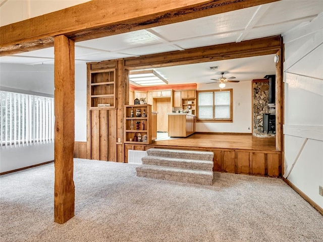 unfurnished living room featuring a wood stove, ceiling fan, and carpet