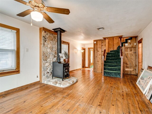 unfurnished living room with a wood stove, ceiling fan, and wood-type flooring