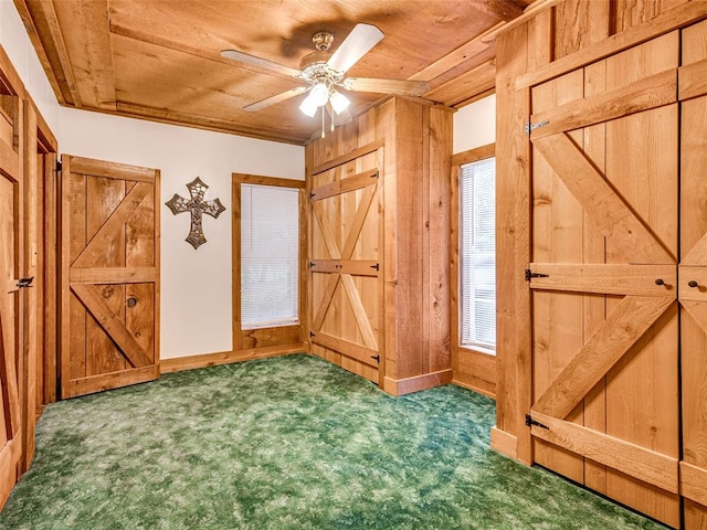 interior space with dark colored carpet, ceiling fan, wood walls, and wooden ceiling