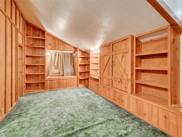 unfurnished living room featuring wooden walls, vaulted ceiling, carpet flooring, built in features, and a textured ceiling