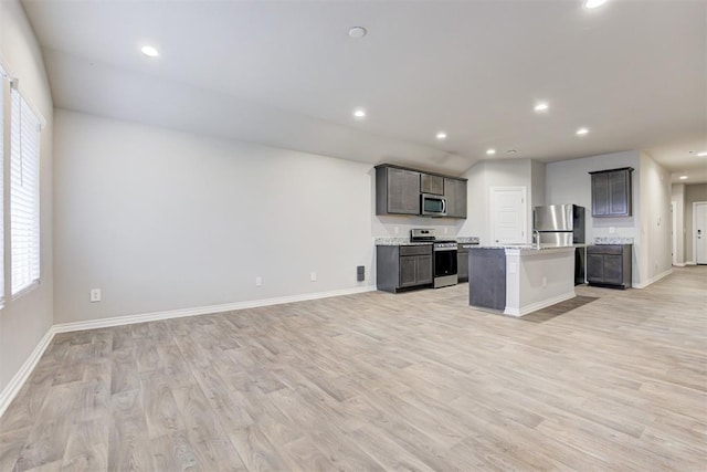 kitchen featuring a kitchen island with sink, light hardwood / wood-style floors, light stone counters, and appliances with stainless steel finishes