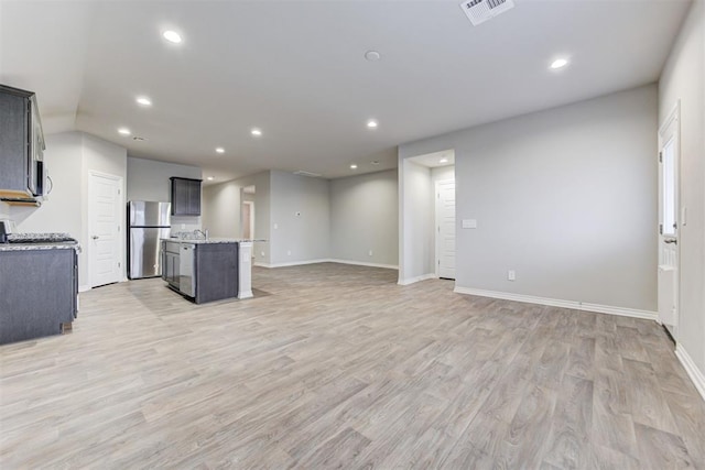 kitchen featuring light stone countertops, a kitchen island with sink, light wood-type flooring, and appliances with stainless steel finishes