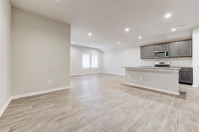 kitchen with light stone counters, light wood-type flooring, stainless steel appliances, and a kitchen island with sink