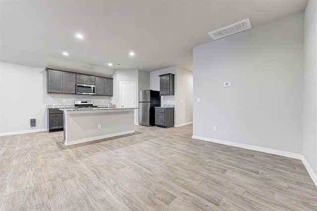 kitchen with gray cabinets, stainless steel appliances, light hardwood / wood-style flooring, and an island with sink