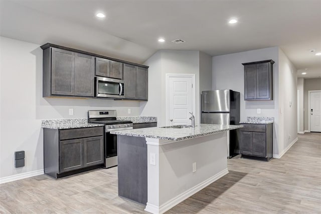 kitchen with light stone countertops, sink, light hardwood / wood-style flooring, a kitchen island with sink, and appliances with stainless steel finishes