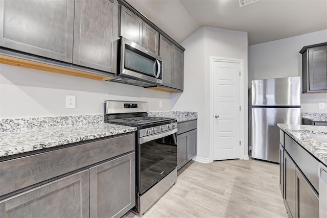 kitchen with dark brown cabinets, light hardwood / wood-style floors, light stone counters, and appliances with stainless steel finishes