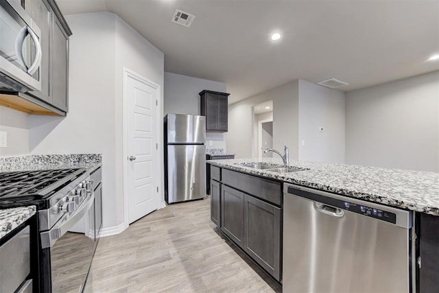 kitchen featuring light stone countertops, light wood-type flooring, stainless steel appliances, and sink