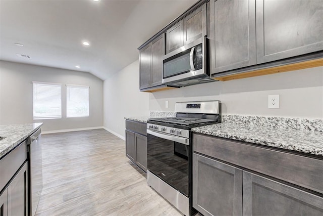 kitchen with vaulted ceiling, appliances with stainless steel finishes, light hardwood / wood-style floors, light stone counters, and dark brown cabinetry