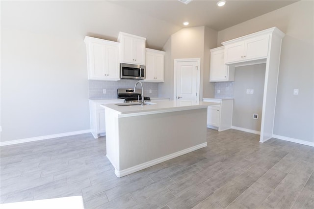 kitchen with white cabinetry, stainless steel appliances, sink, and a center island with sink