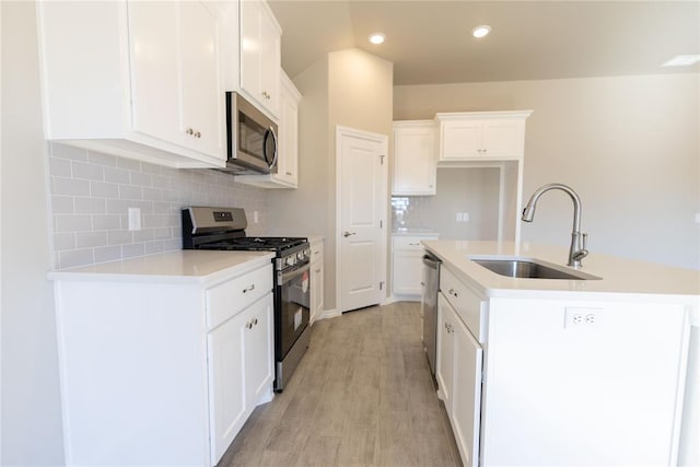 kitchen featuring appliances with stainless steel finishes, white cabinetry, sink, decorative backsplash, and a center island with sink