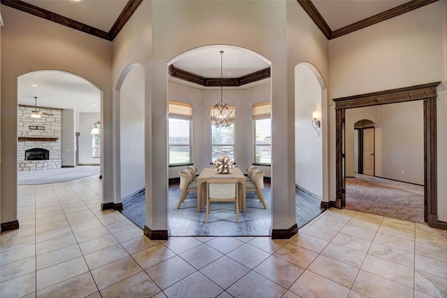 unfurnished dining area with light tile patterned floors, an inviting chandelier, a stone fireplace, and crown molding