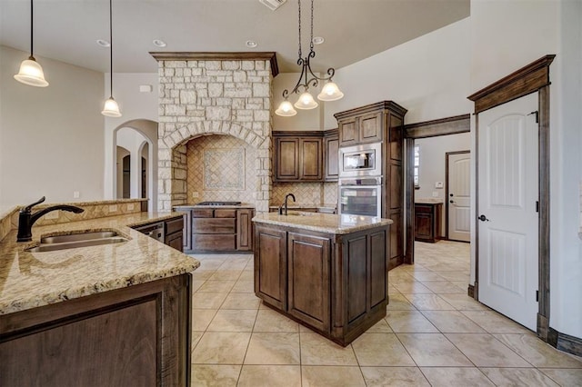 kitchen with a center island with sink, sink, light stone countertops, appliances with stainless steel finishes, and decorative light fixtures