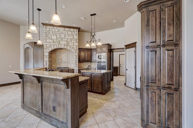 kitchen with backsplash, a center island with sink, appliances with stainless steel finishes, decorative light fixtures, and light stone counters