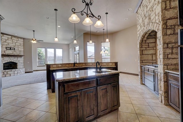 kitchen featuring a kitchen island with sink, a fireplace, a sink, open floor plan, and hanging light fixtures