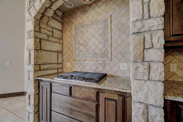 kitchen featuring light stone countertops, stainless steel gas cooktop, dark brown cabinetry, and light tile patterned floors