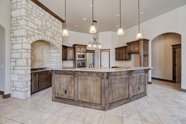 kitchen with arched walkways, stainless steel appliances, light stone countertops, a large island with sink, and pendant lighting