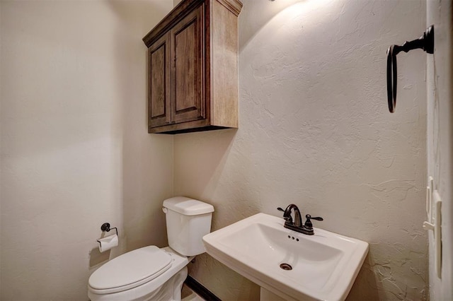 half bathroom featuring toilet, a sink, and a textured wall