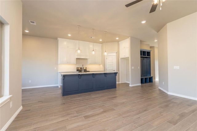 kitchen with pendant lighting, light wood-type flooring, white cabinetry, and an island with sink