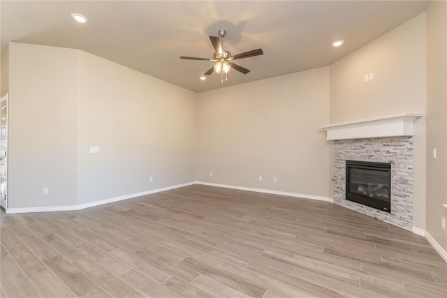 unfurnished living room featuring light hardwood / wood-style floors, a stone fireplace, and ceiling fan