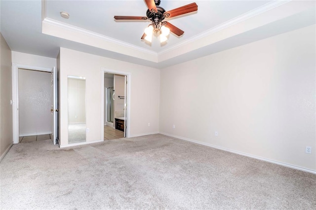 unfurnished bedroom featuring ceiling fan, ensuite bathroom, light colored carpet, a tray ceiling, and ornamental molding