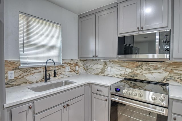 kitchen with gray cabinetry, light stone countertops, sink, stainless steel appliances, and backsplash