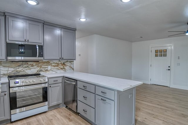 kitchen with light stone countertops, light wood-type flooring, tasteful backsplash, kitchen peninsula, and stainless steel appliances