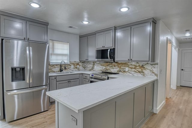 kitchen with light stone counters, sink, light hardwood / wood-style flooring, and appliances with stainless steel finishes