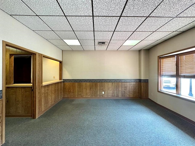 carpeted spare room with wooden walls and a drop ceiling