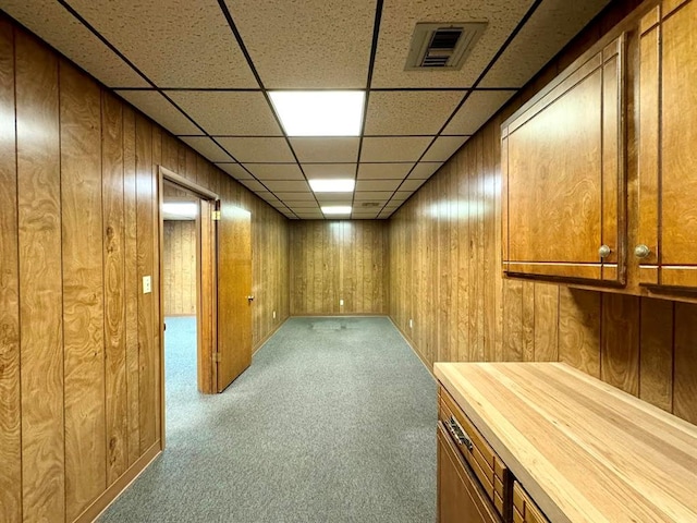 basement featuring wooden walls, a drop ceiling, and carpet