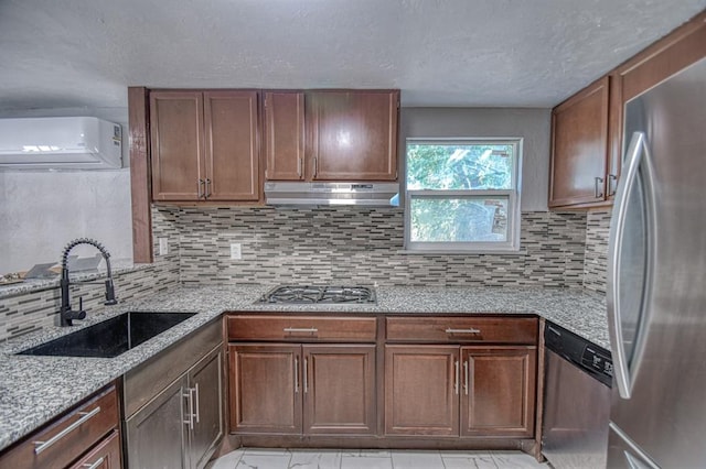 kitchen featuring decorative backsplash, appliances with stainless steel finishes, light stone counters, a wall unit AC, and sink