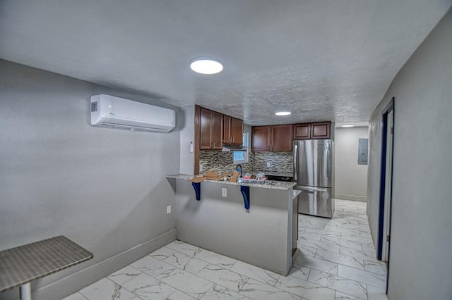 kitchen with kitchen peninsula, a kitchen bar, a wall mounted air conditioner, backsplash, and stainless steel refrigerator