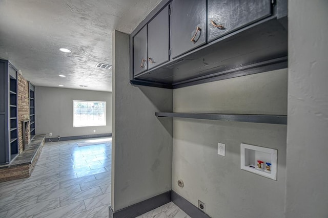 laundry area with cabinets, electric dryer hookup, a stone fireplace, hookup for a washing machine, and a textured ceiling