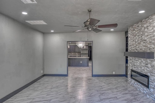 unfurnished living room featuring ceiling fan with notable chandelier and a fireplace