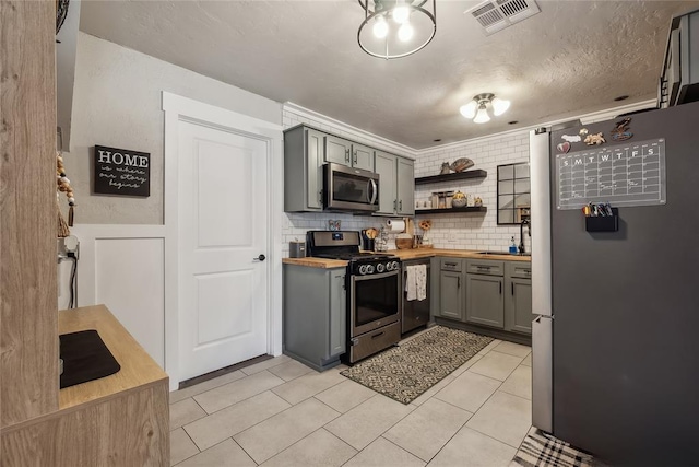 kitchen featuring gray cabinetry, wood counters, a textured ceiling, decorative backsplash, and appliances with stainless steel finishes