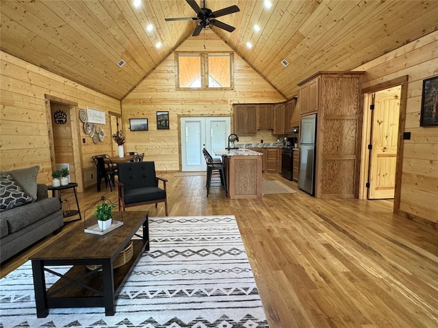 living room with sink, light hardwood / wood-style floors, wood ceiling, and wood walls