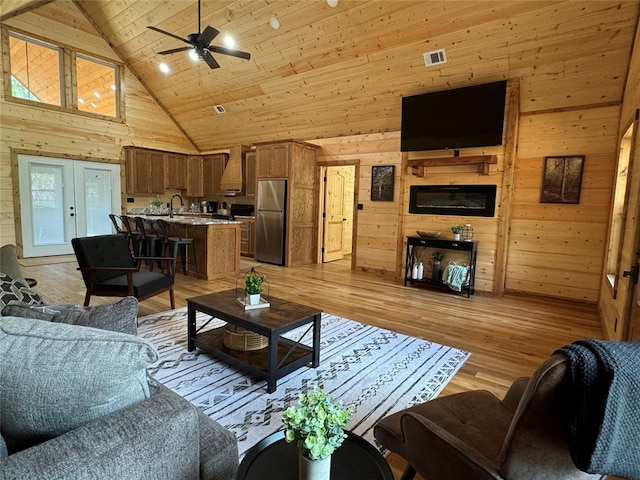 living room with ceiling fan, wood walls, light hardwood / wood-style floors, and high vaulted ceiling