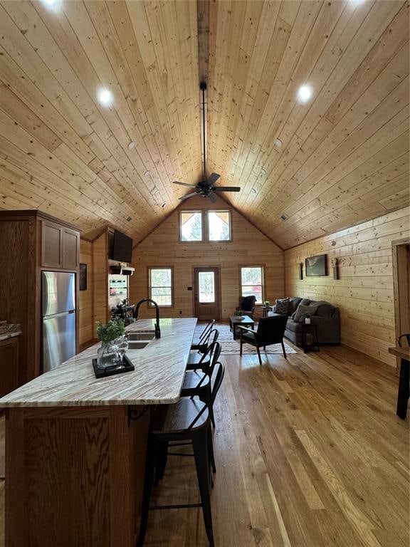 kitchen featuring stainless steel refrigerator, sink, wooden ceiling, light hardwood / wood-style flooring, and wooden walls