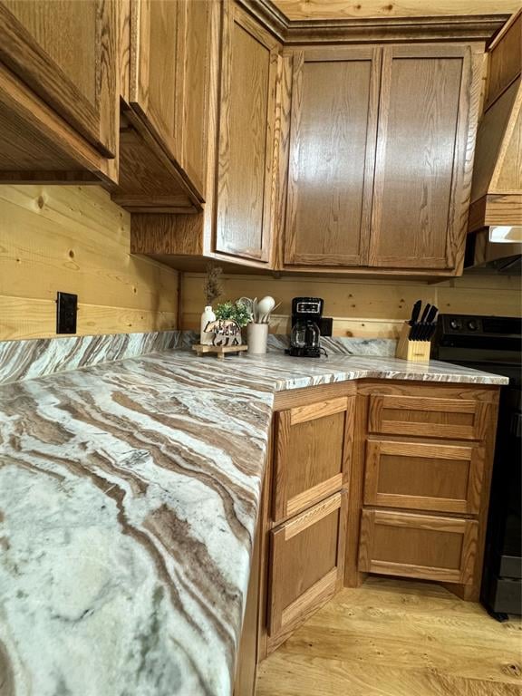 kitchen with custom range hood, electric range, light hardwood / wood-style floors, and wooden walls