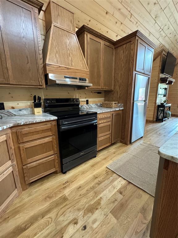 kitchen with stainless steel fridge, custom exhaust hood, wooden walls, light hardwood / wood-style flooring, and black range with electric stovetop