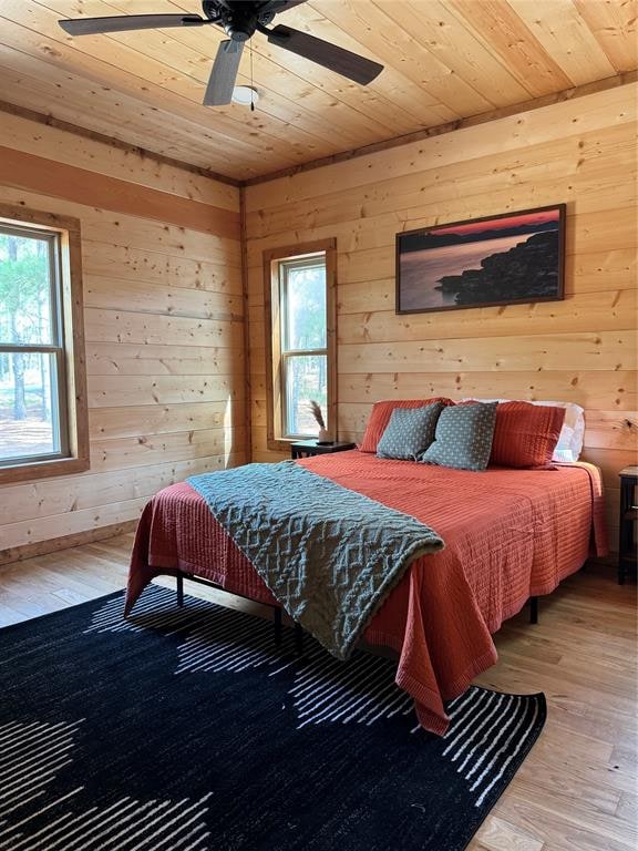 bedroom featuring multiple windows, ceiling fan, wood walls, and hardwood / wood-style flooring