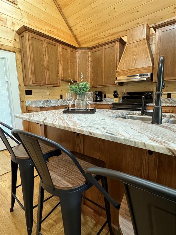 kitchen featuring a kitchen breakfast bar, light wood-type flooring, premium range hood, light stone counters, and lofted ceiling